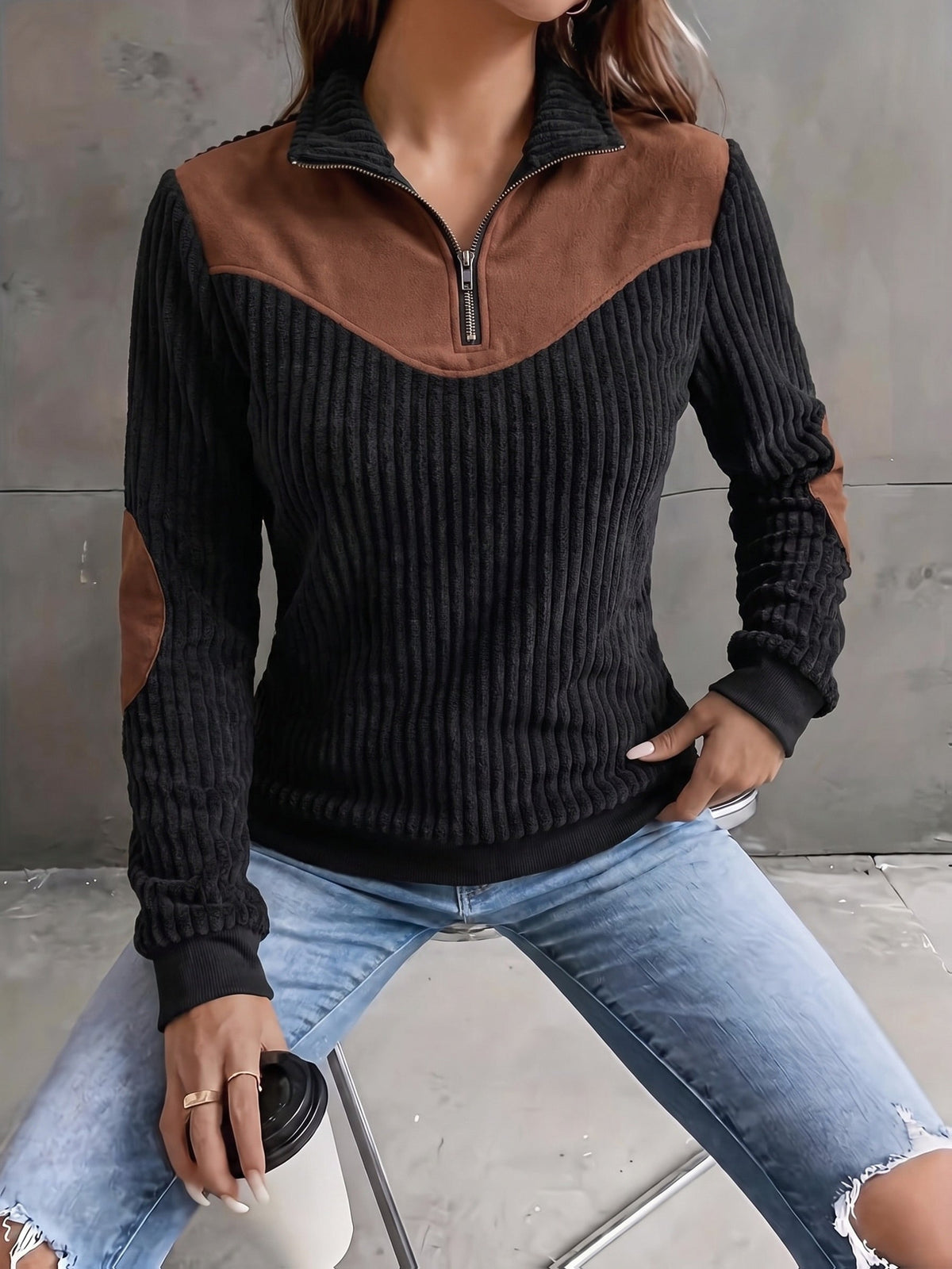 Black ribbed knit quarter-zip sweater featuring a brown suede-look yoke and matching elbow patches, worn with distressed jeans.