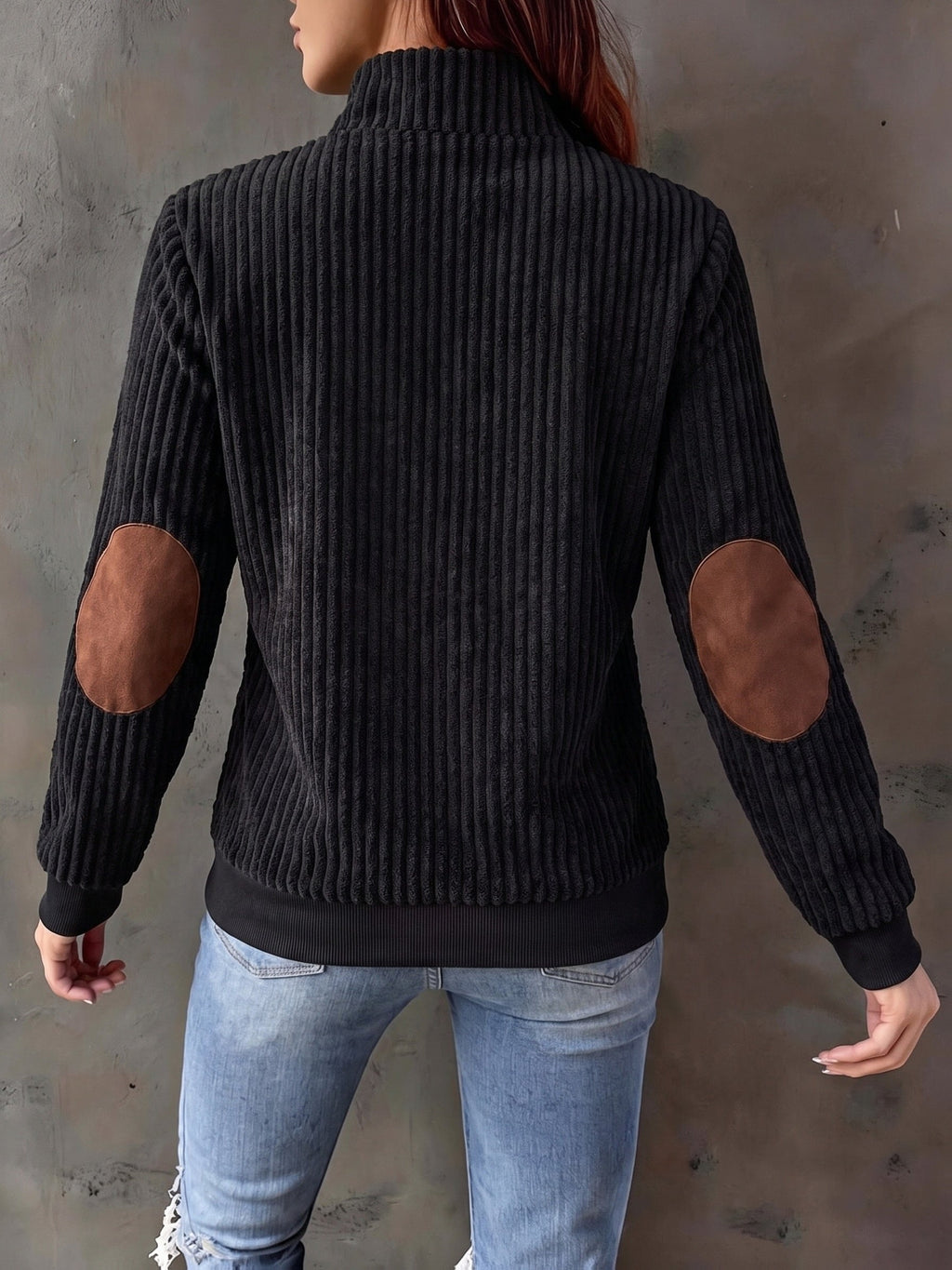 Black ribbed knit quarter-zip sweater with brown suede-look elbow patches and a stand collar worn with blue jeans.