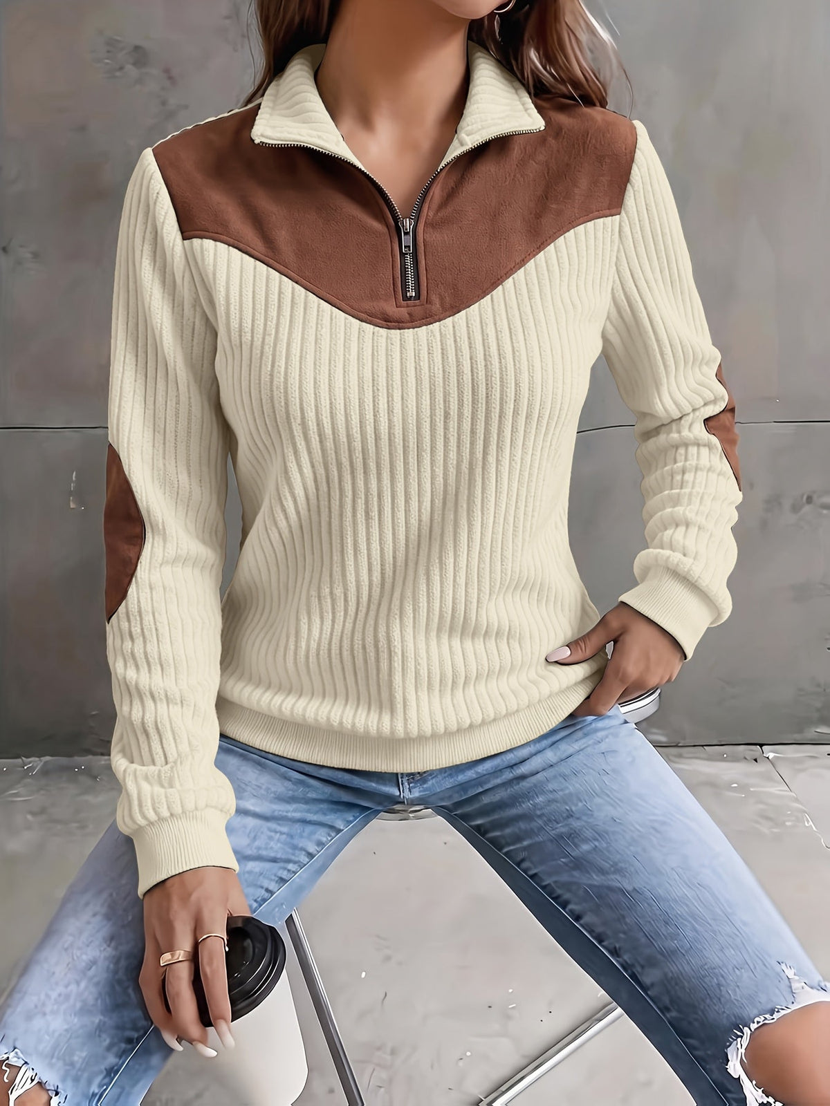 Cream ribbed knit quarter-zip sweater with brown suede-look yoke and matching elbow patches, styled with distressed jeans.