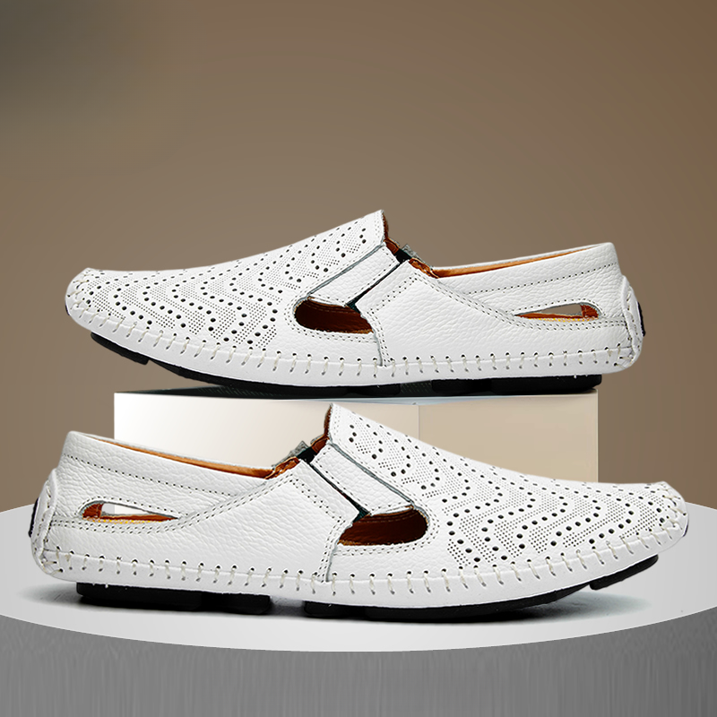 Pair of white perforated leather slip-on sandals with hand-stitched trim, one shoe stacked on a white display block above the other.