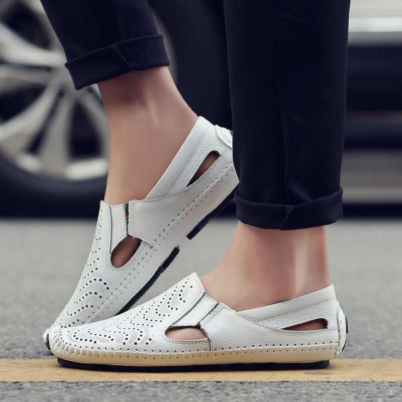 Close-up of a model's feet wearing white perforated leather slip-on sandals with hand-stitched trim while standing outdoors on pavement.