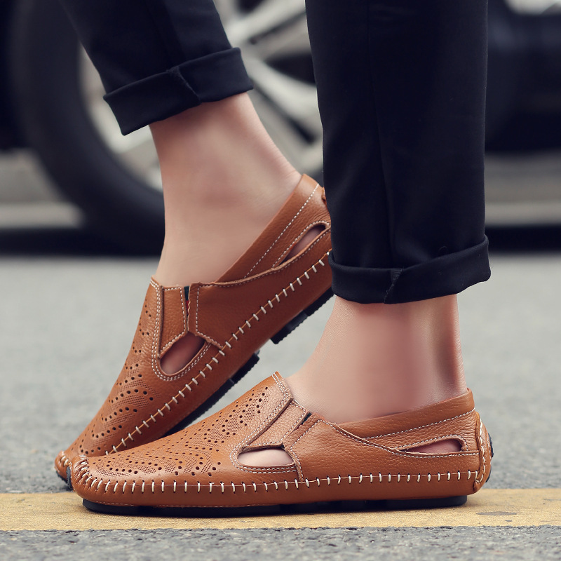 Close-up of a model's feet wearing brown perforated leather slip-on sandals with hand-stitched trim while standing outdoors on pavement.