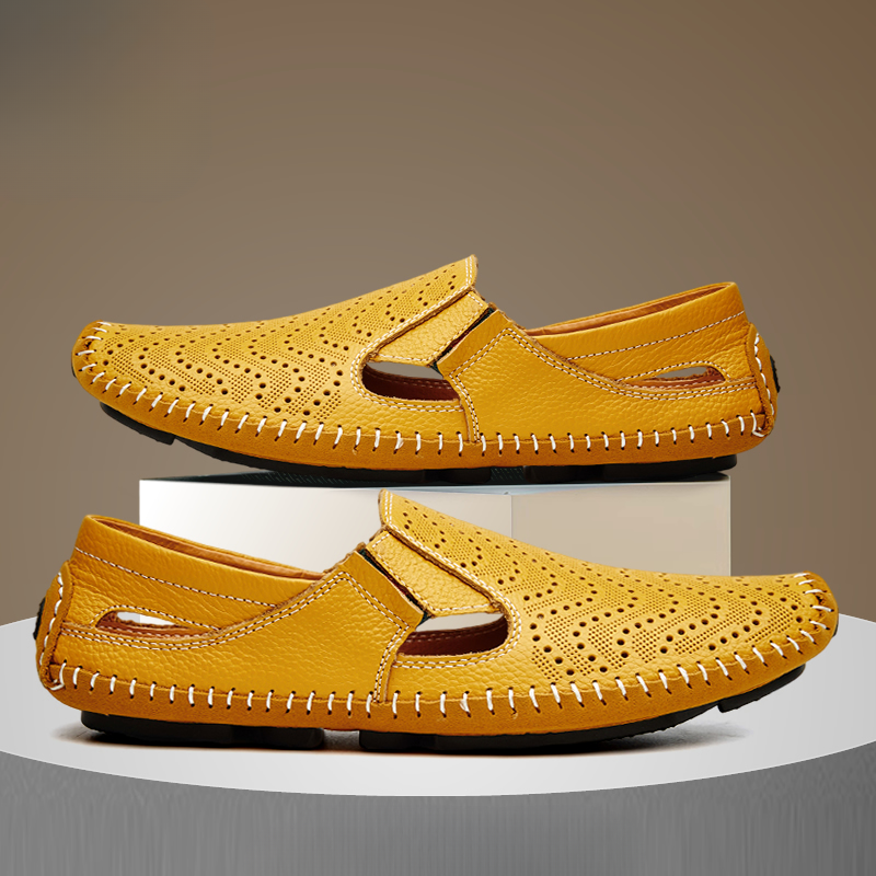 Pair of yellow perforated leather slip-on sandals with hand-stitched trim, one shoe stacked on a white display block above the other.