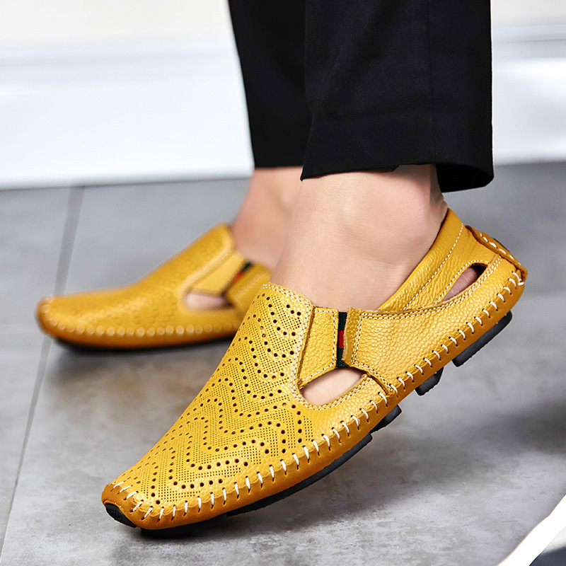 Close-up of a model's feet wearing yellow perforated leather slip-on sandals with hand-stitched trim while standing on tiled flooring.