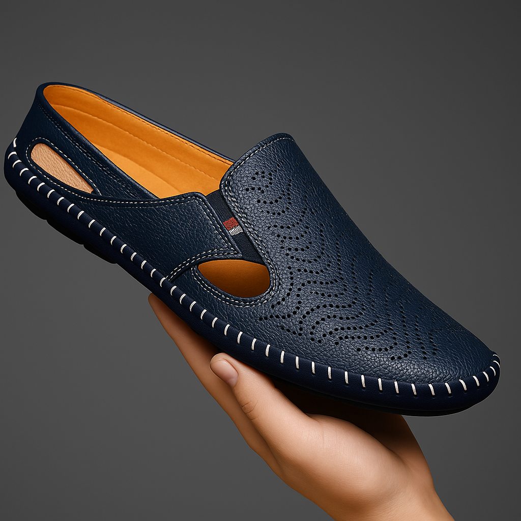 Hand holding a navy blue perforated leather slip-on sandal with hand-stitched trim and a side cutout, showing the orange interior lining.