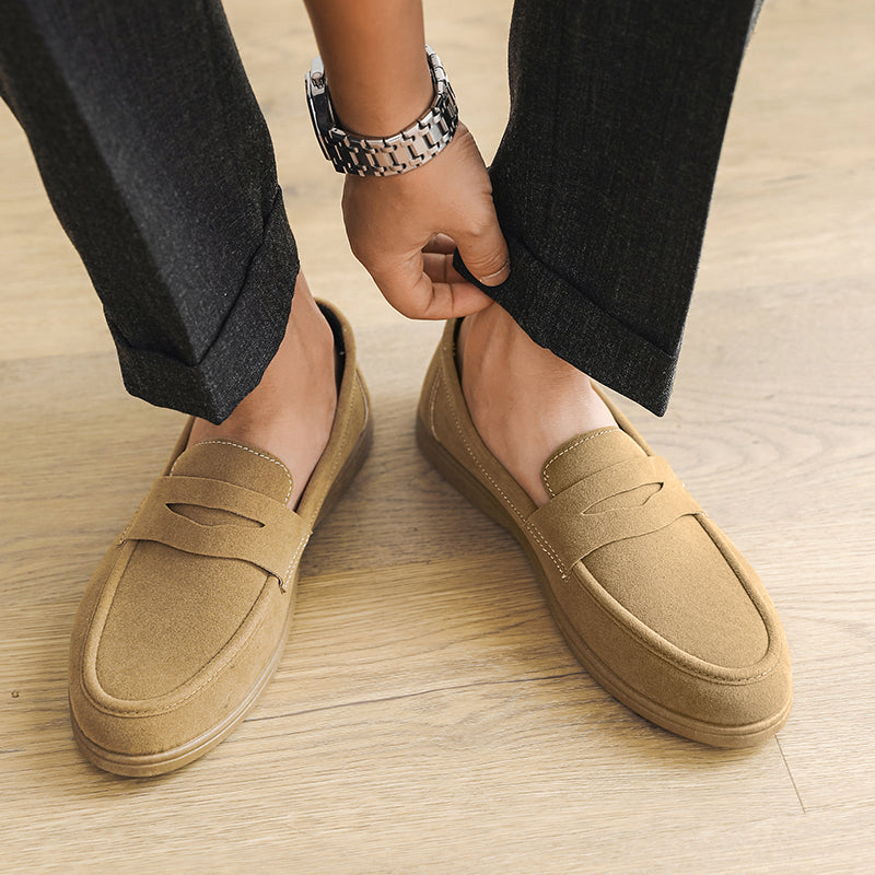 Overhead view of a person adjusting cuffed gray trousers while wearing tan suede loafers, standing on a wood floor.