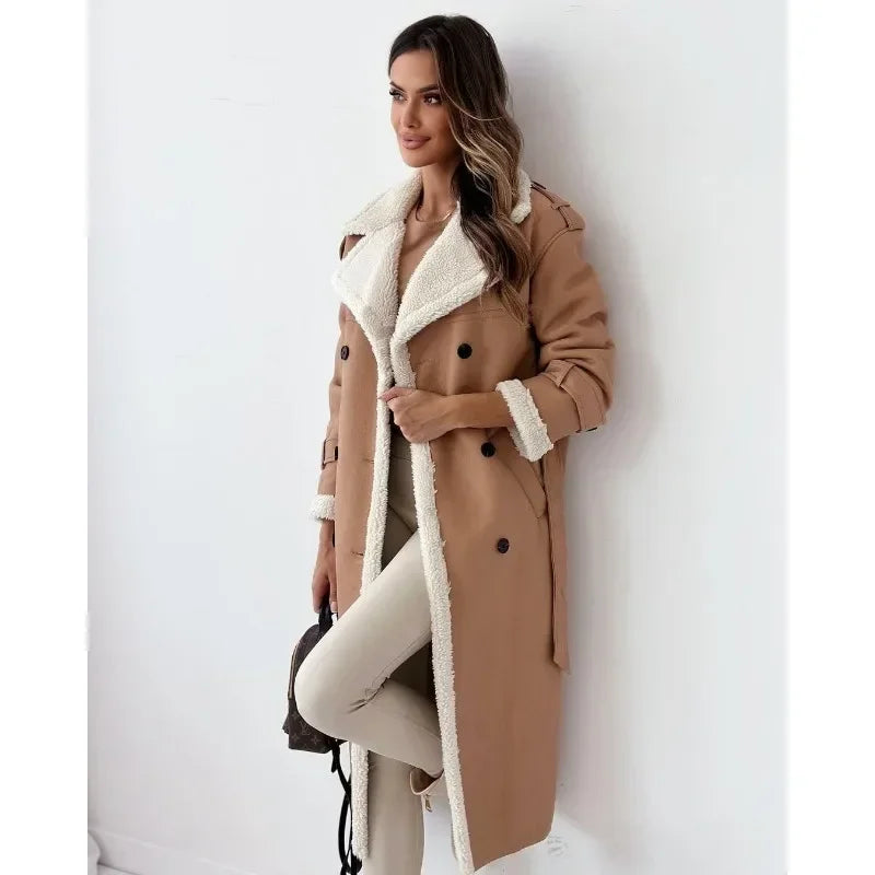 Tan shearling trench coat with cream teddy lining, double-breasted buttons, and a belted waist in a longline silhouette.