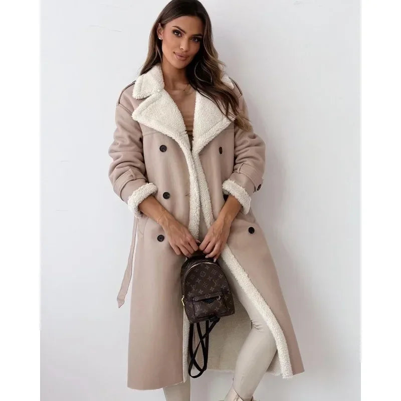 Beige shearling trench coat with cream teddy lining, double-breasted buttons, and a belted waist in a longline silhouette.