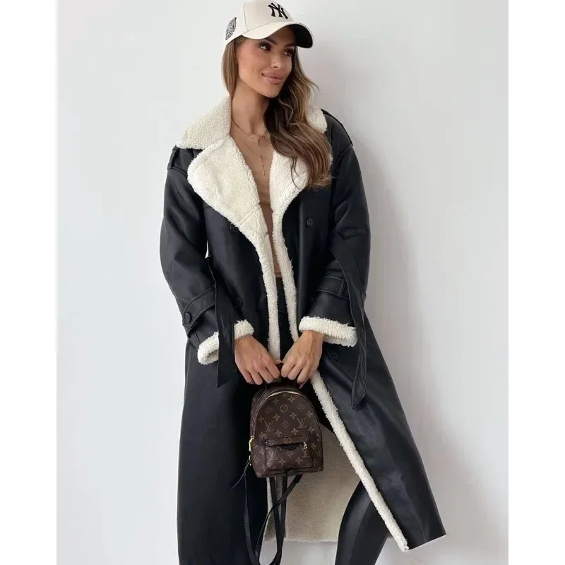 Black longline trench coat with cream teddy lining, wide collar, and belted waist, worn with a baseball cap.