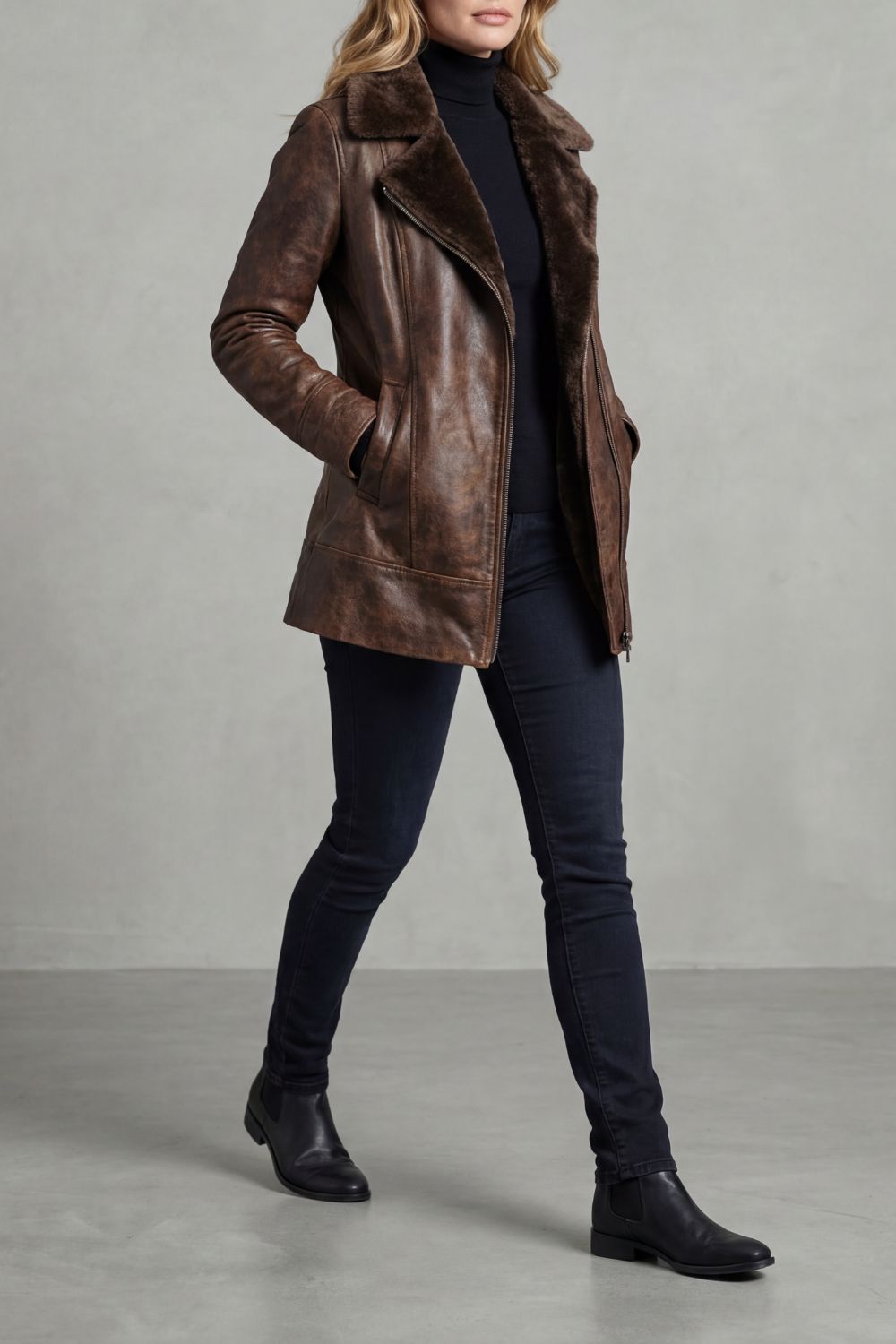 Brown vegan leather jacket with a plush shearling collar, tailored fit, and zip front worn over dark jeans.