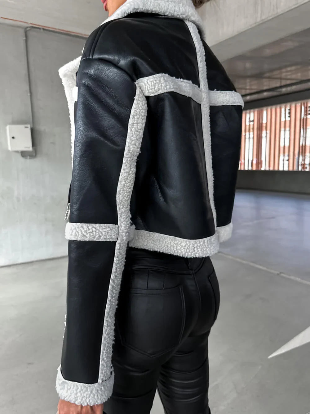 Black vegan leather cropped aviator jacket with white sherpa trim, seam detailing, and a structured fit.
