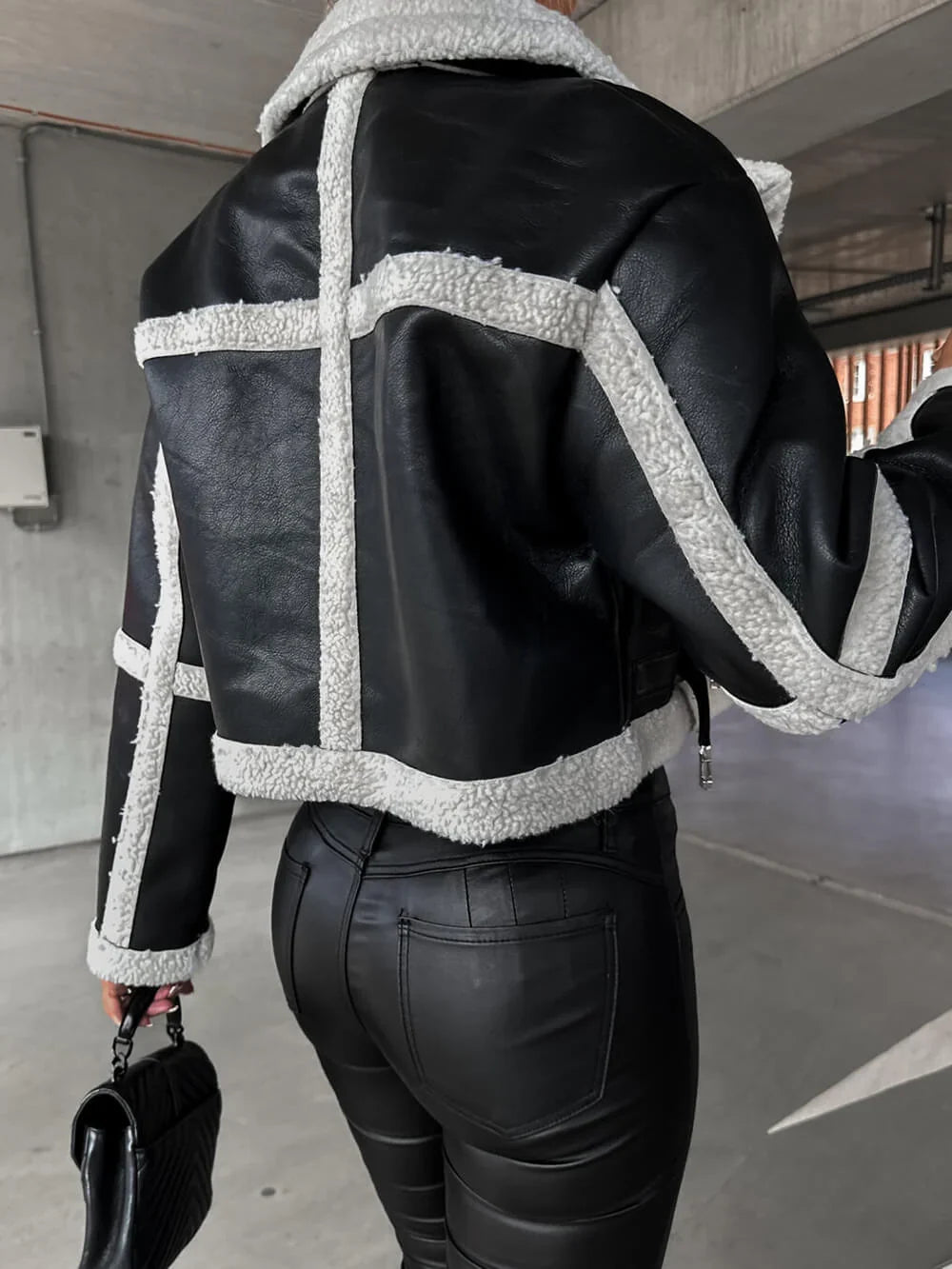 Black vegan leather cropped aviator jacket with white sherpa trim, featuring structured seams and a waist-length fit.