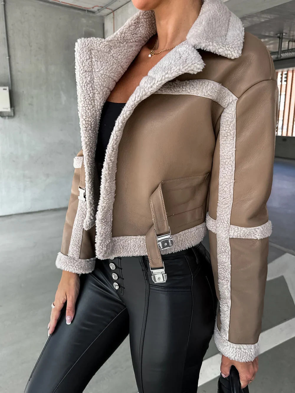 Cropped beige vegan leather aviator jacket with plush cream sherpa trim, seam detailing, and adjustable waist buckles.