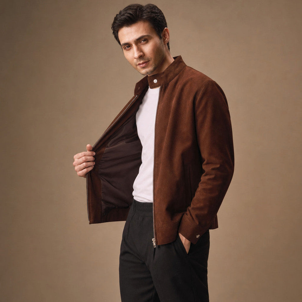 A man wearing a brown suede bomber jacket with a full-zip front and snap band collar, standing indoors