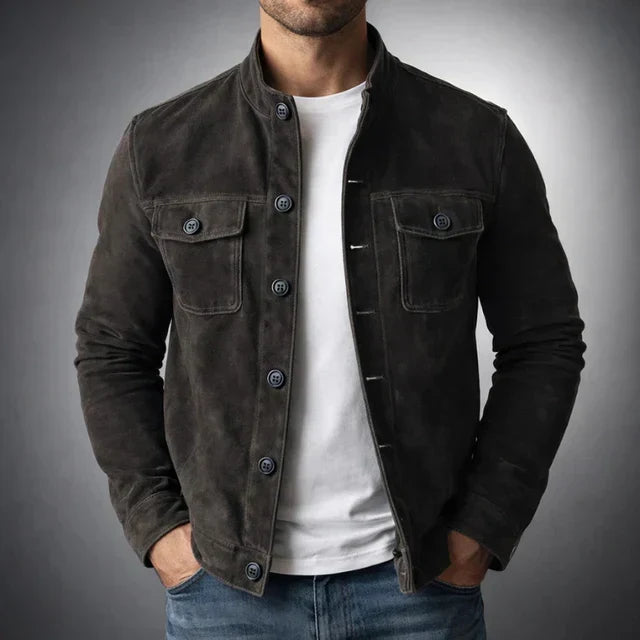 A man wearing a black suede jacket with button closure and chest pockets, standing indoors