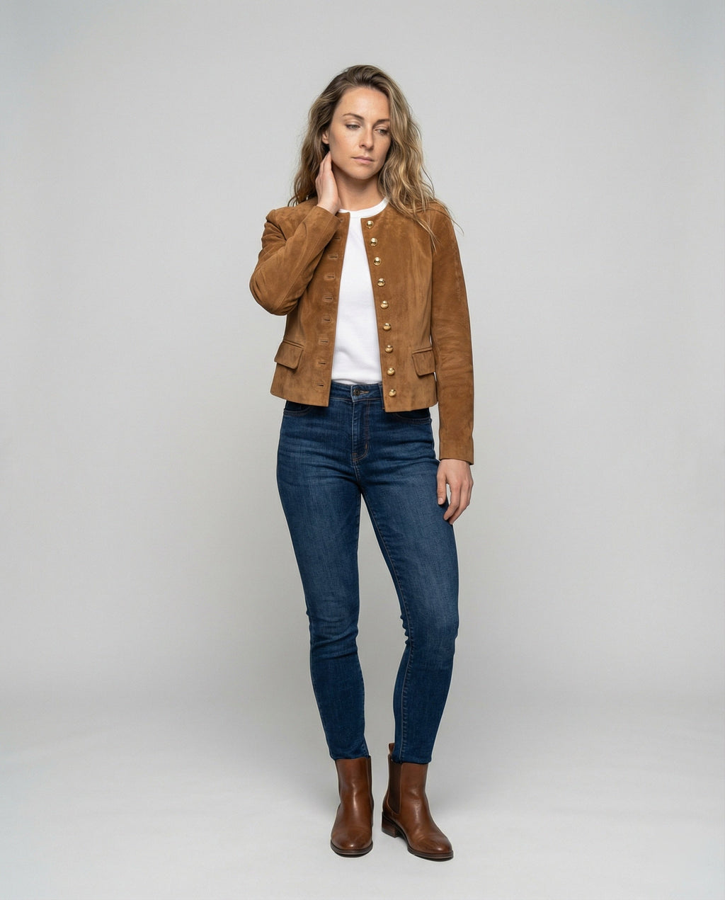 A woman wearing a brown suede cropped jacket with a collarless design, gold-tone buttons, and fitted cut, full-length view