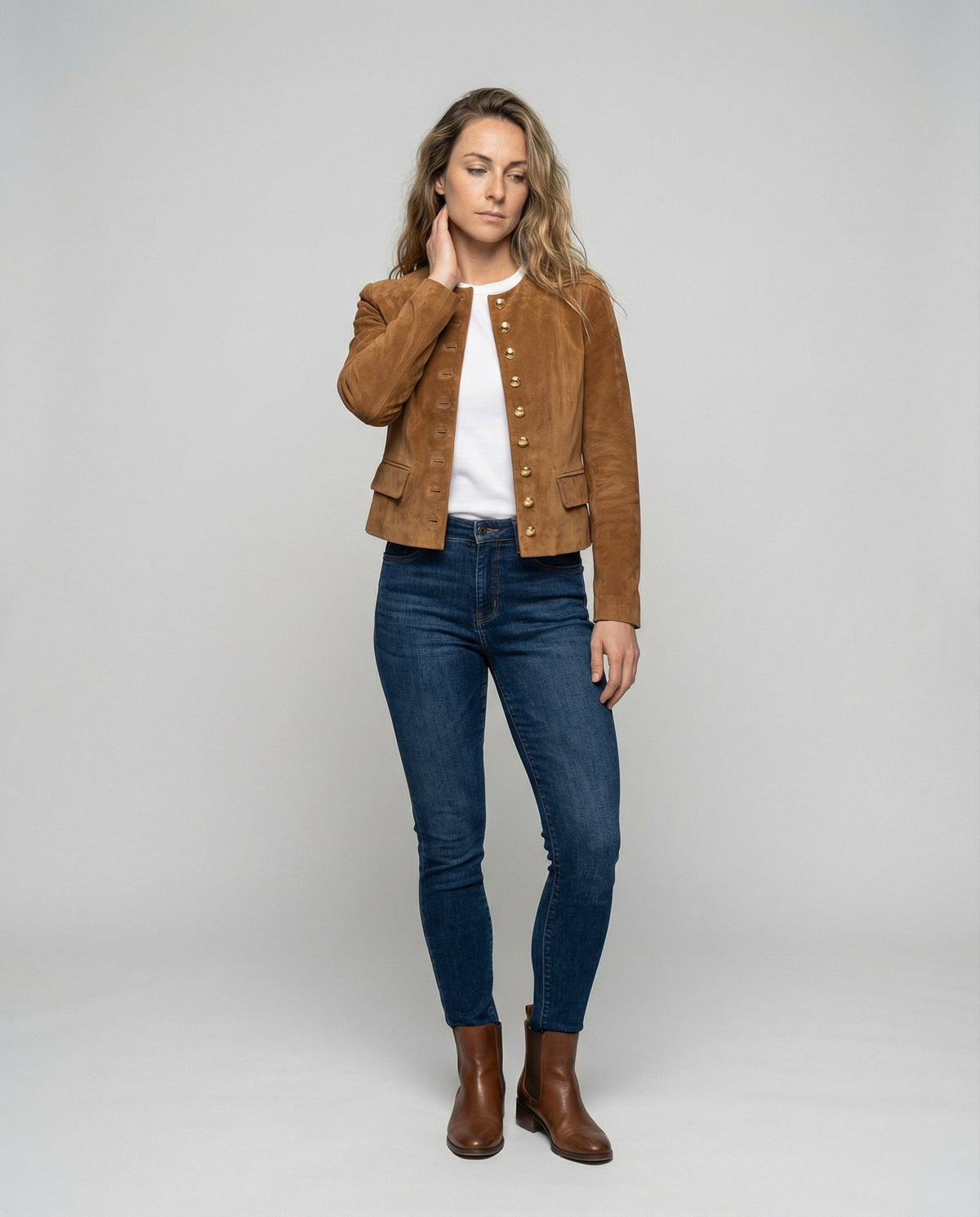 A woman wearing a brown suede cropped jacket with a collarless design, gold-tone buttons, and fitted cut, full-length view