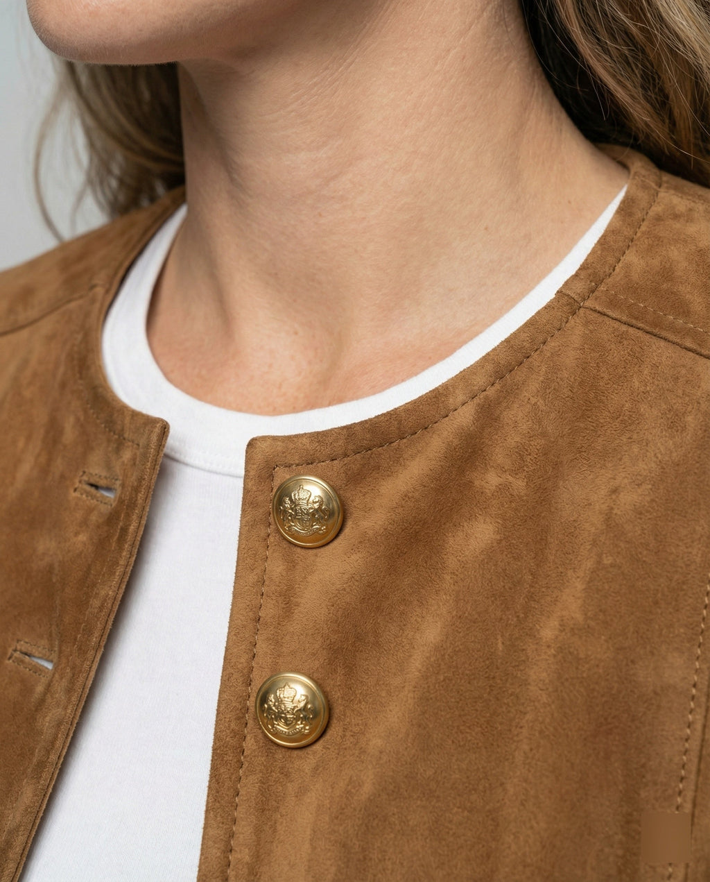 Close-up of a brown suede cropped jacket showing the collarless neckline and gold-tone buttons
