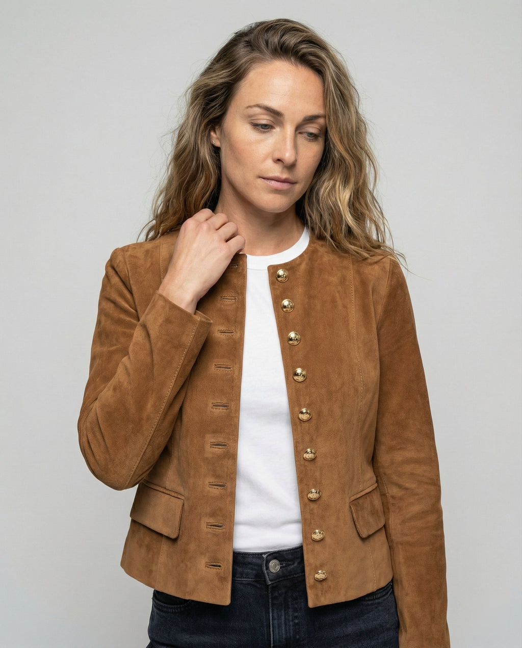 A woman wearing a brown suede cropped jacket with a collarless design, gold-tone buttons, and fitted cut