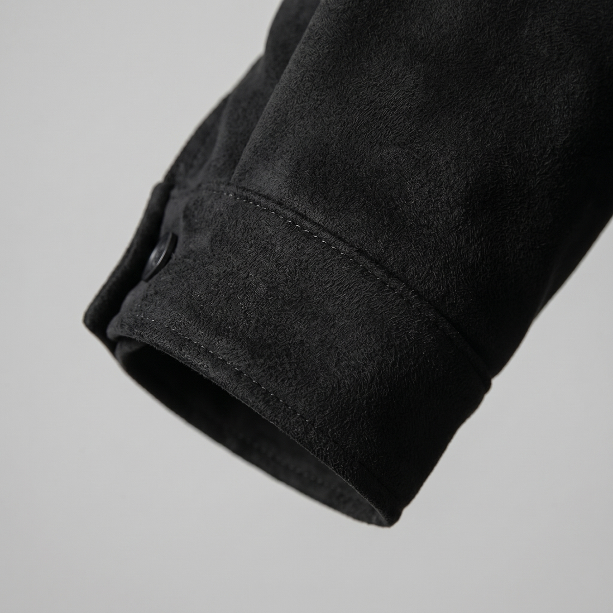 Close-up of a black suede Harrington bomber jacket showing the ribbed sleeve cuff and suede texture
