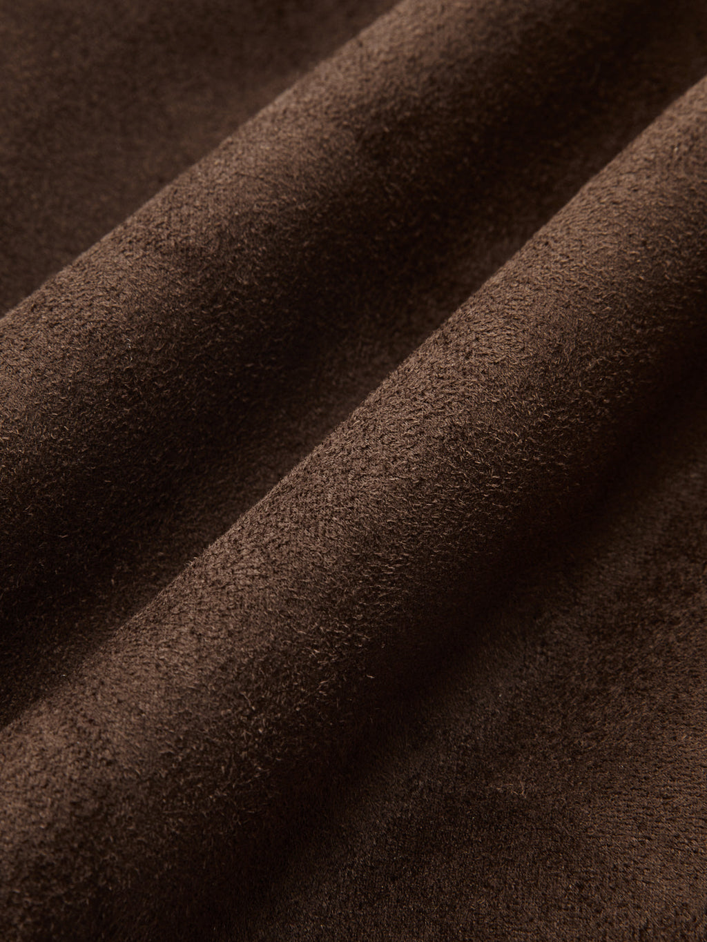 Close-up of rich dark brown vegan suede fabric with a soft, brushed matte texture and gentle folds.