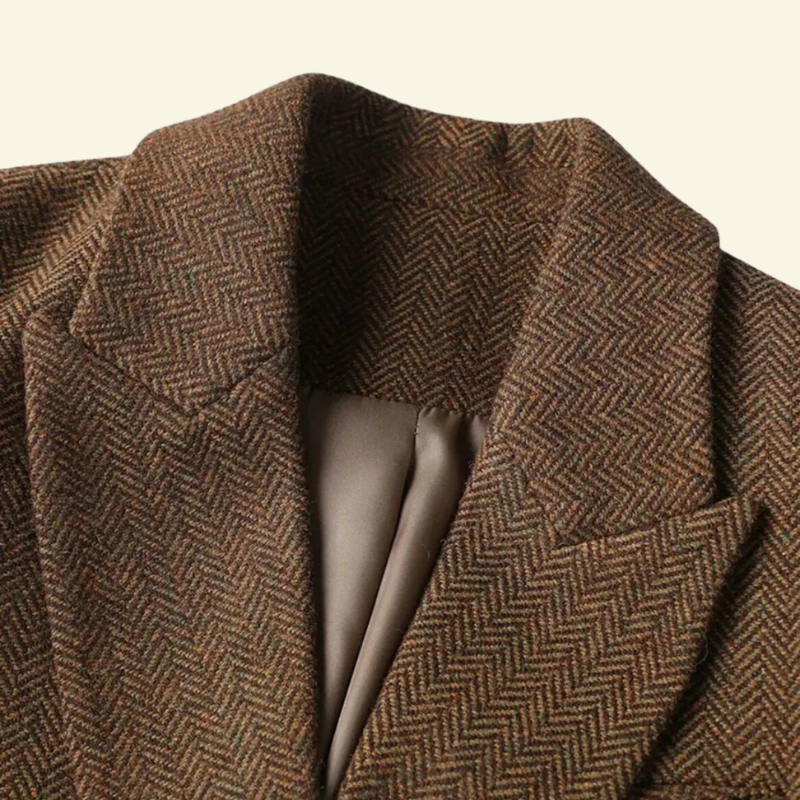 Close-up of the brown blazer showing the notched lapel, textured herringbone fabric, and structured tailoring.