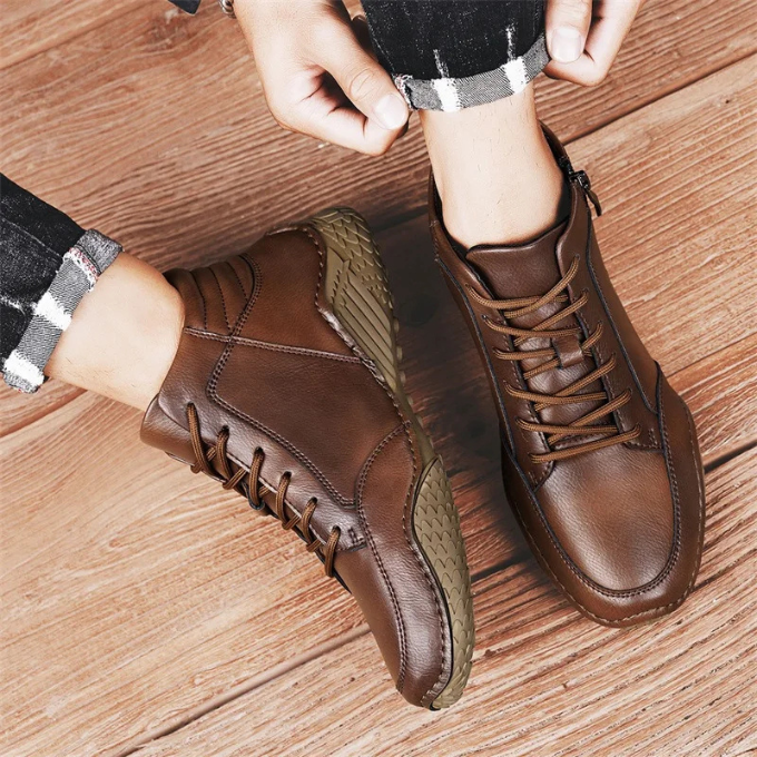 Overhead view of a person adjusting cuffed plaid-lined pants over brown leather zip-up ankle boots with olive green accents, on a wooden floor.