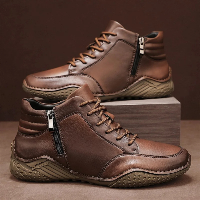 Pair of brown full-grain leather zip-up ankle boots with lug soles, resting against a stone block on a brown backdrop.