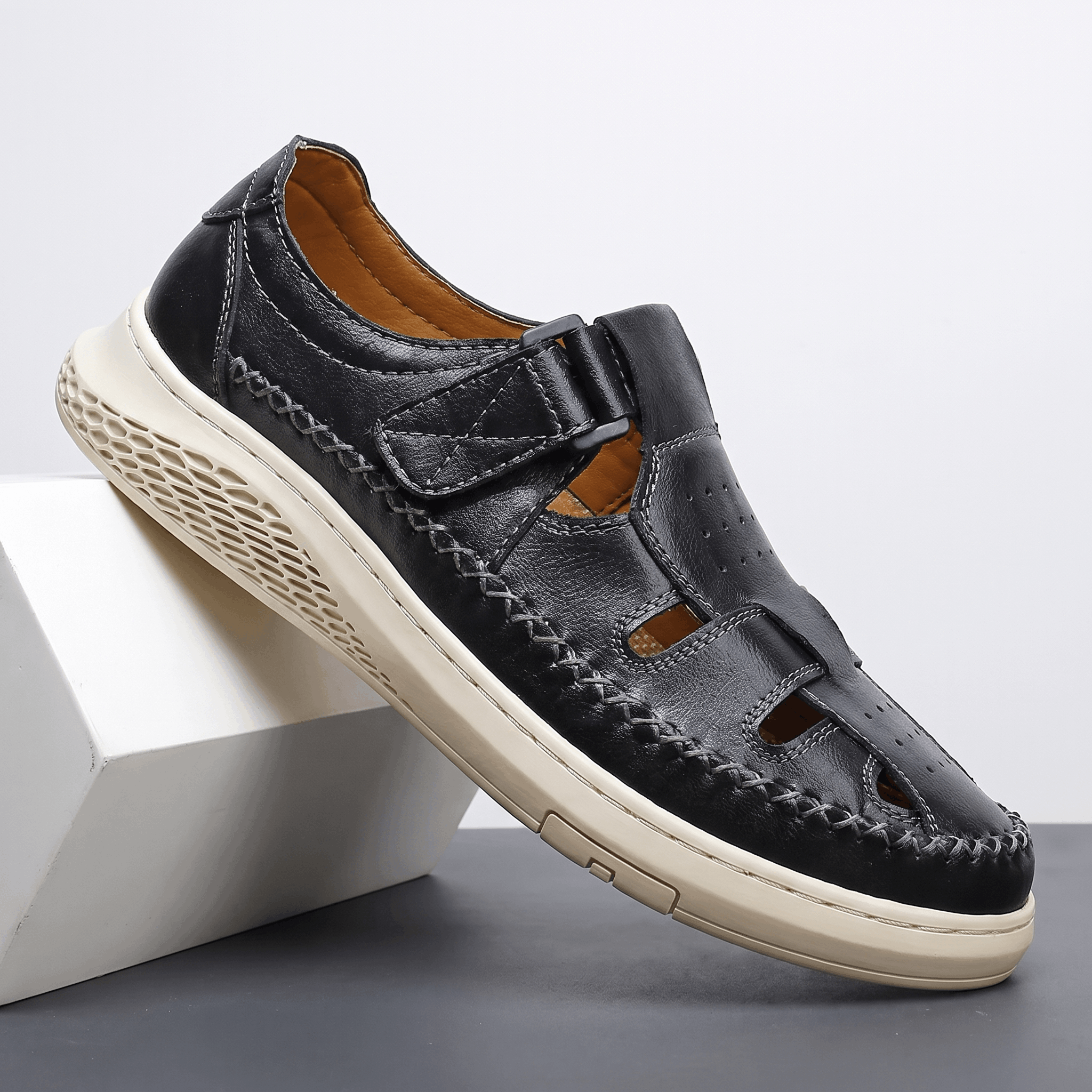 Single black leather Toby fisherman sandal with cutout panels and chunky white sole, angled on a white block against a studio backdrop