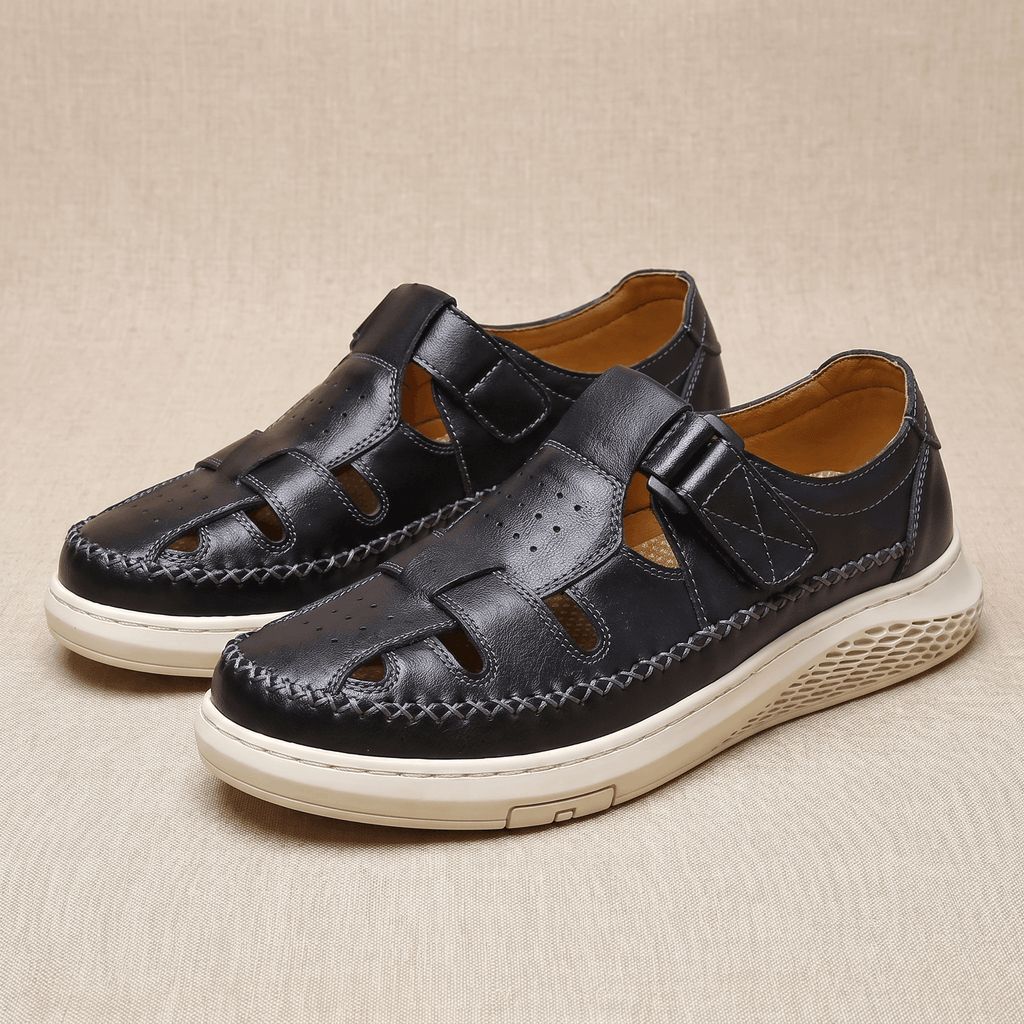 Pair of black leather Toby fisherman sandals with cutout panels, resting on a beige fabric backdrop