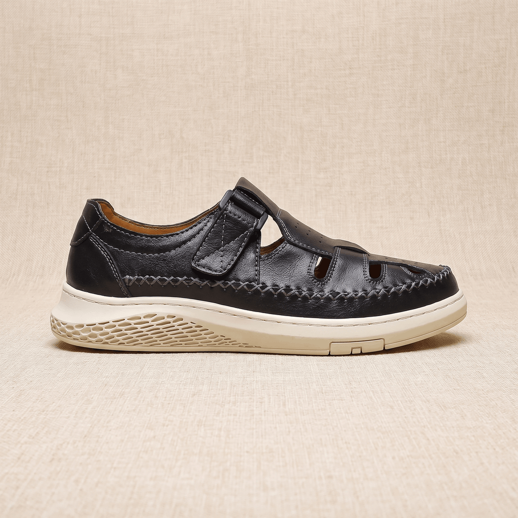 Side view of a single black leather Toby fisherman sandal with strap closure, resting on a beige surface