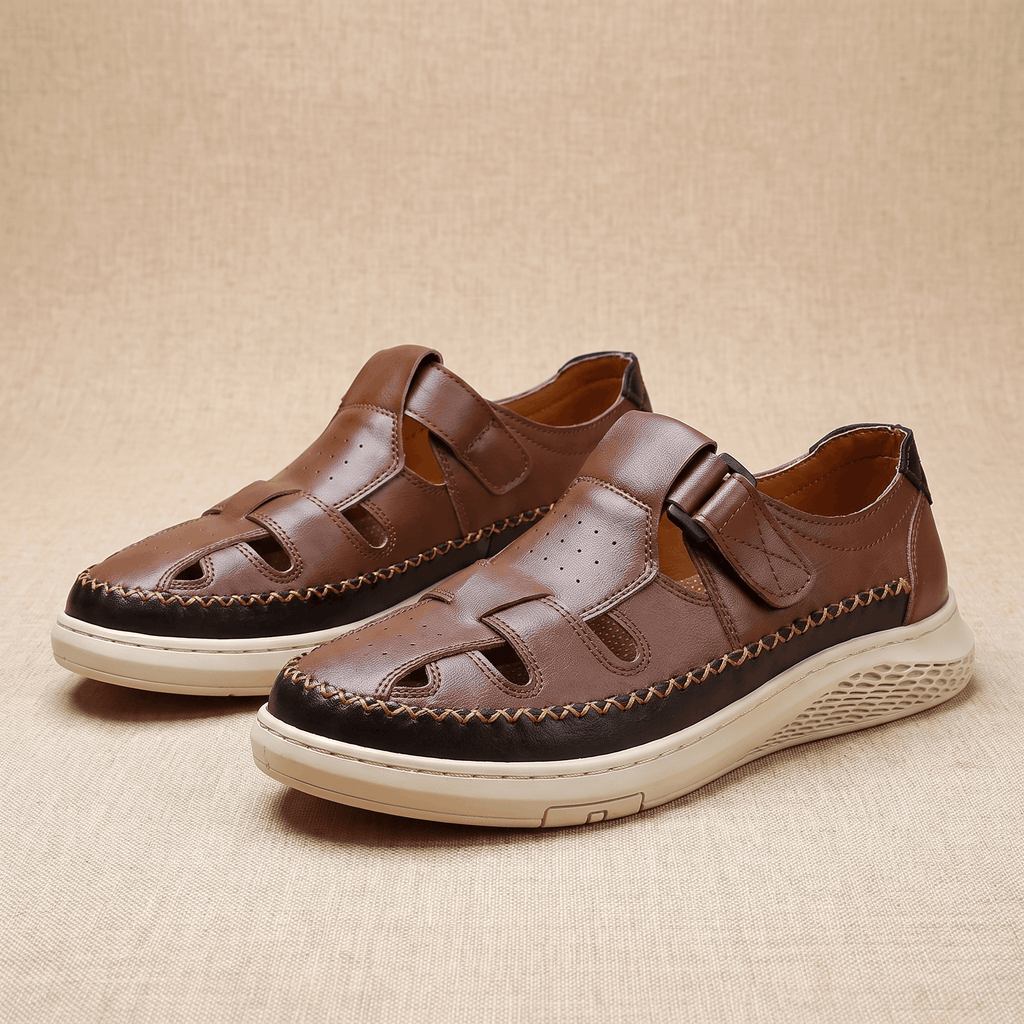 Pair of brown leather Toby fisherman sandals with cutout panels and hook-and-loop straps, resting on a beige fabric backdrop