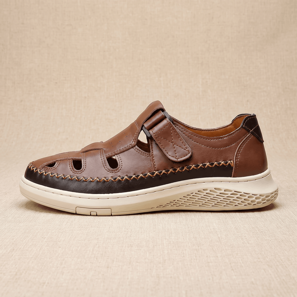 Side profile of a single brown leather Toby fisherman sandal with hook-and-loop strap and cutout panels, resting on a beige surface