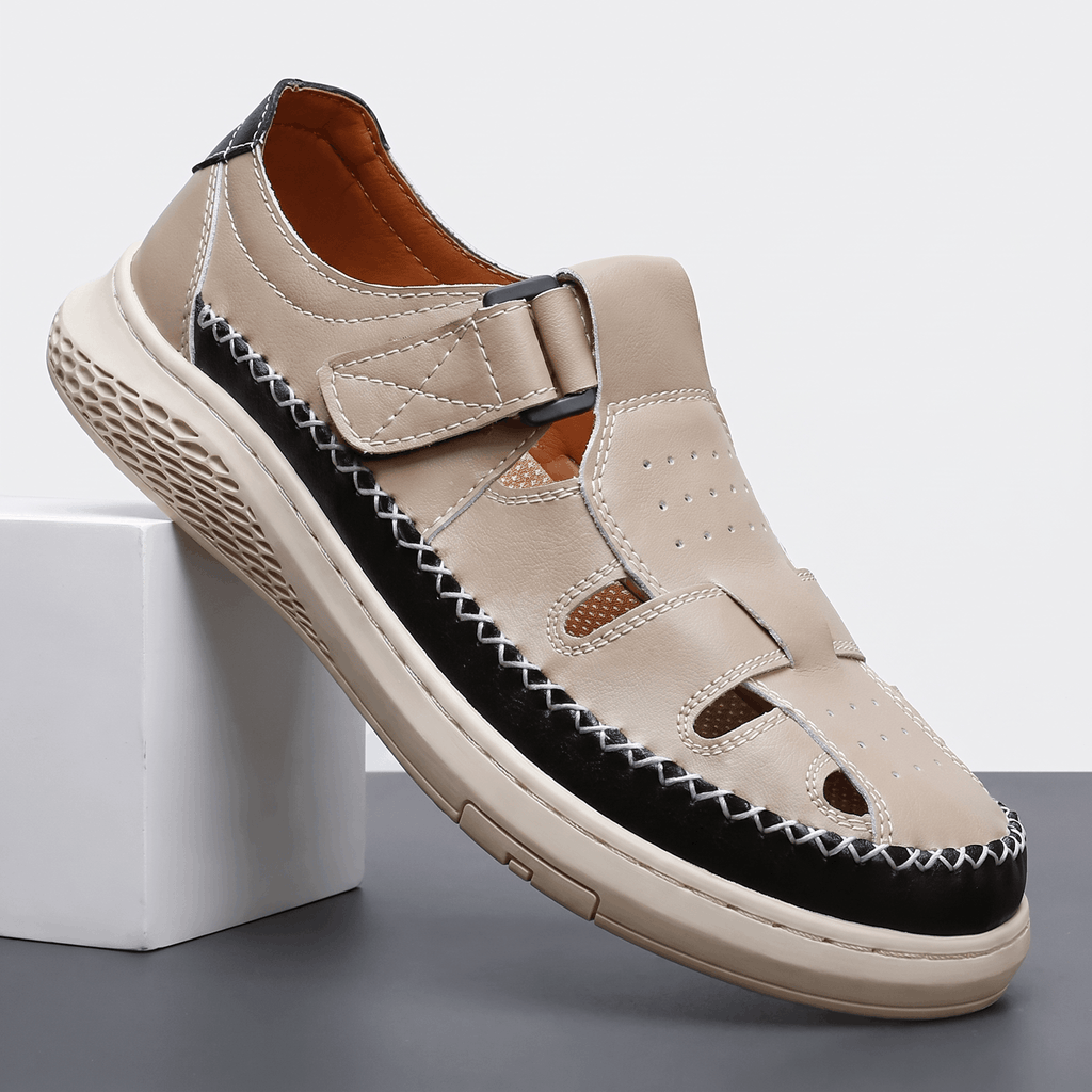 Single beige leather Toby fisherman sandal with black trim and cutout panels, angled on a white block against a studio backdrop