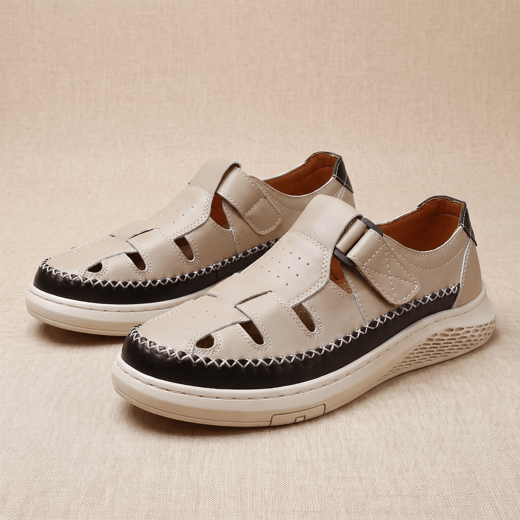 Pair of beige leather Toby fisherman sandals with black trim, resting on a beige fabric backdrop