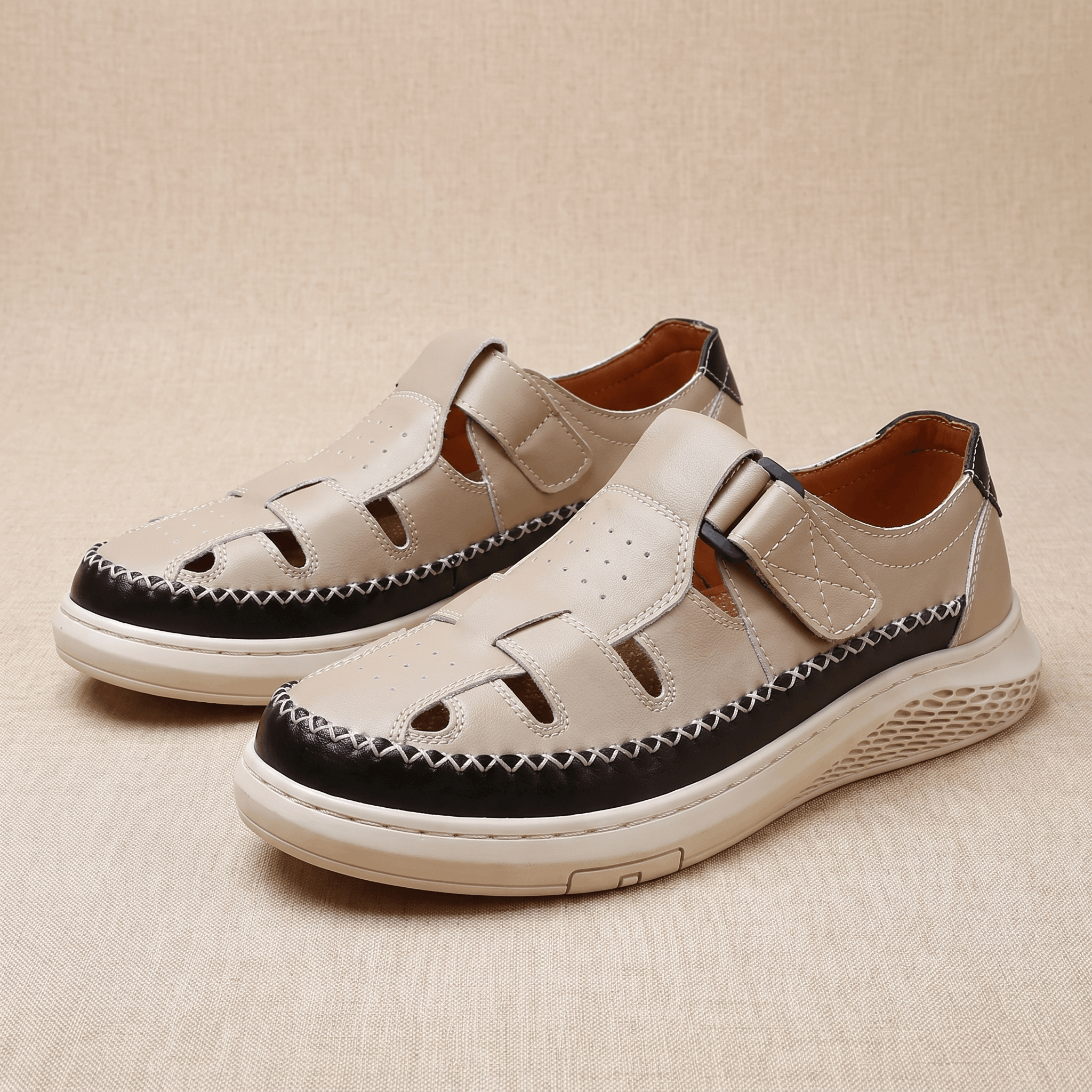 Pair of beige leather Toby fisherman sandals with black trim, resting on a beige fabric backdrop
