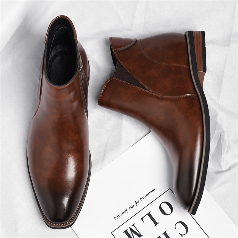 Overhead view of a pair of brown leather Chelsea boots with side zippers, lying on a white sheet beside a magazine.