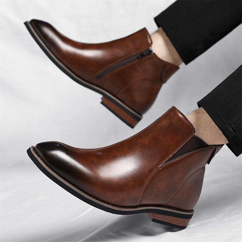 A model's ankles in black trousers wearing brown leather Chelsea boots with side zippers, one foot lifted mid-step on a white sheet.