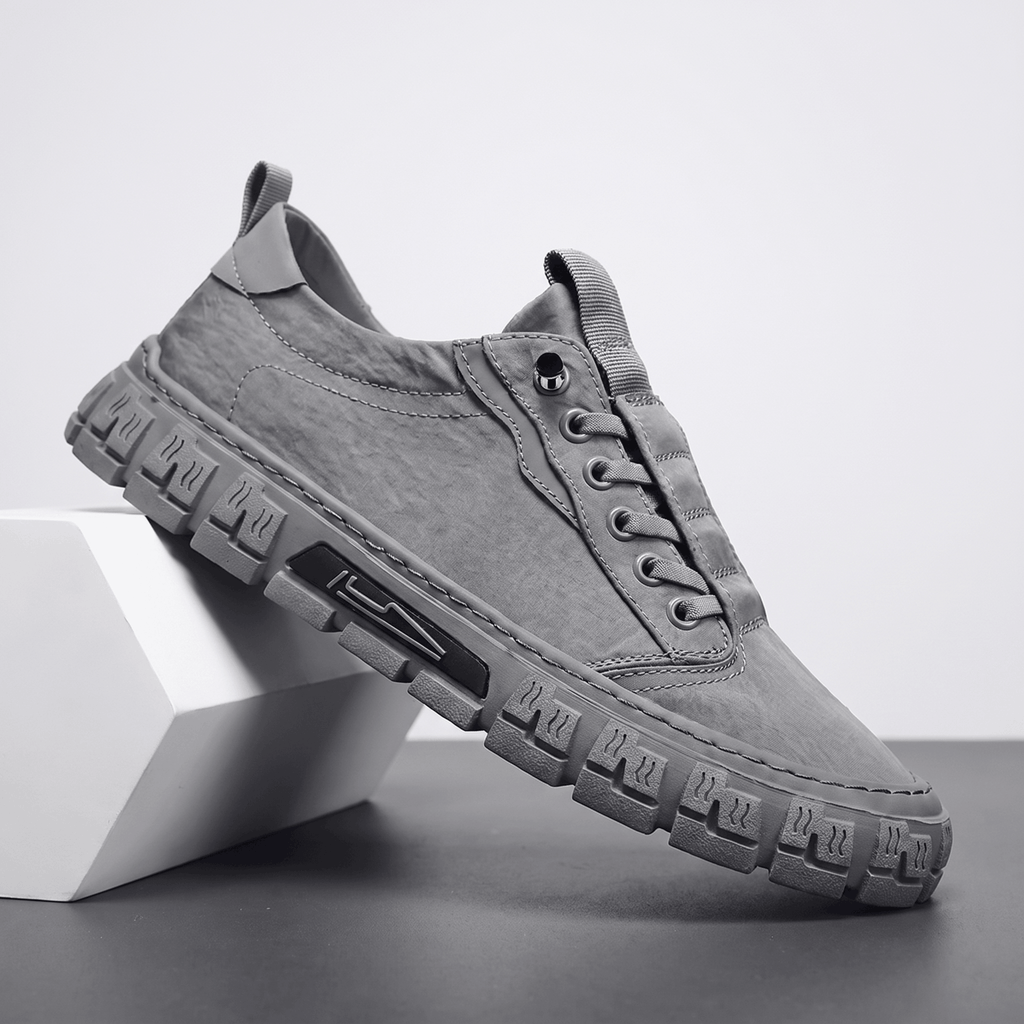 Gray canvas sneaker with matching sole propped diagonally against a white geometric block in a studio setting