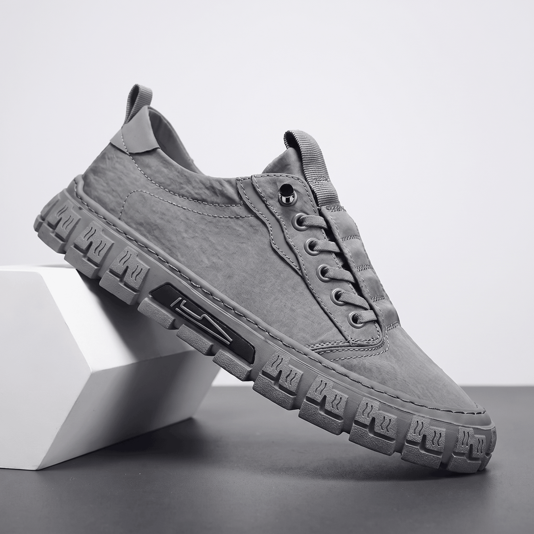 Gray canvas sneaker with matching sole propped diagonally against a white geometric block in a studio setting