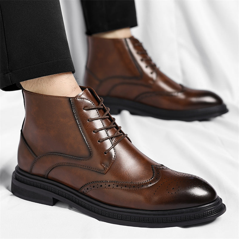 A model's ankles in cropped black trousers wearing brown leather brogue lace-up boots, standing on a white sheet.