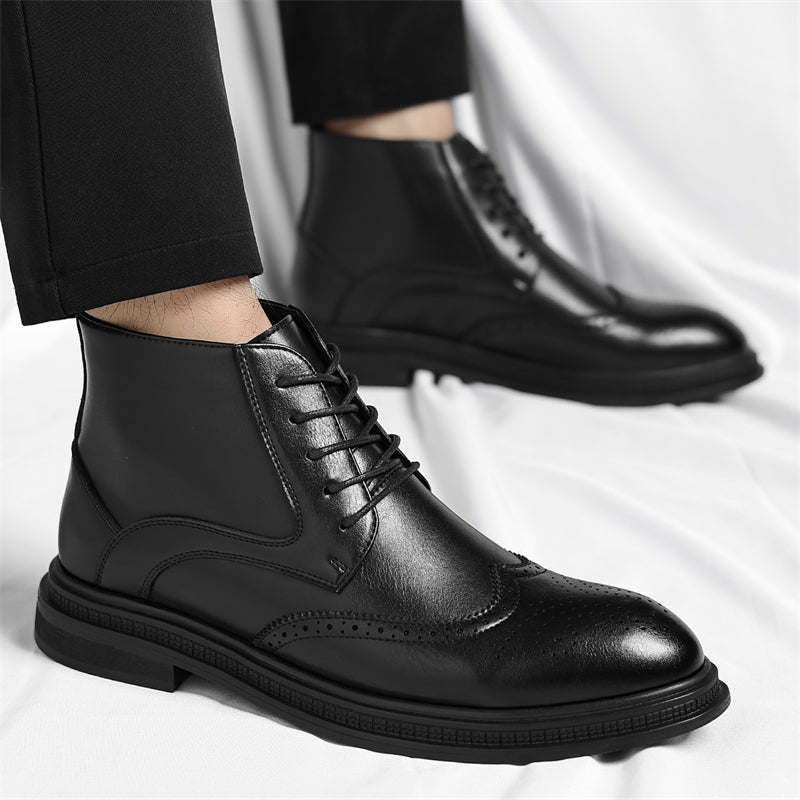 Close-up of a model's ankles in black trousers wearing black leather brogue boots, standing on a white sheet.