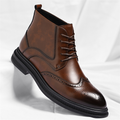 A brown leather brogue lace-up ankle boot with wingtip perforation detailing, shown on a white sheet.