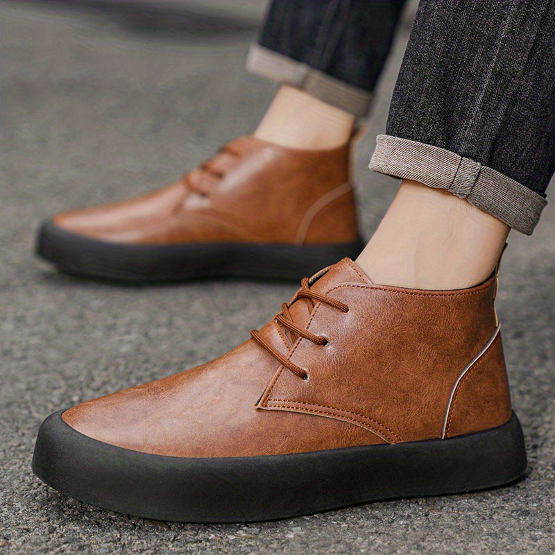 A person walking on concrete pavement wearing brown leather chukka-style boots and cuffed dark gray trousers.