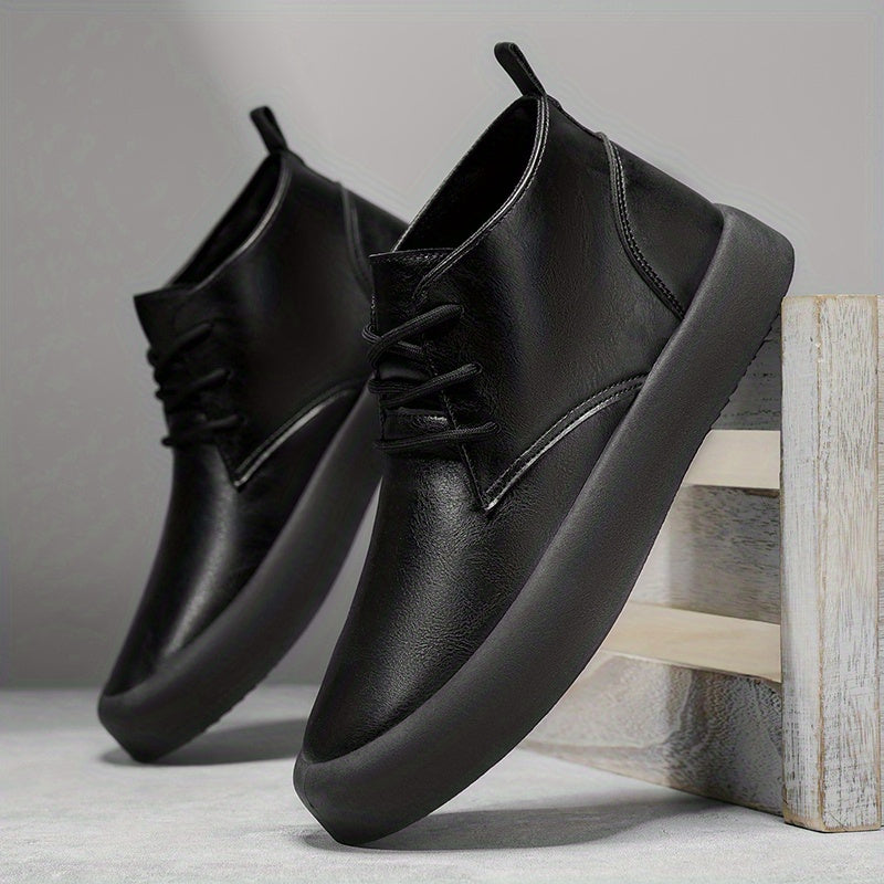 Pair of black leather chukka-style boots leaning against a wooden crate on a textured concrete surface.