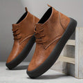 Pair of brown leather chukka-style boots leaning against a wooden crate on a textured concrete surface.