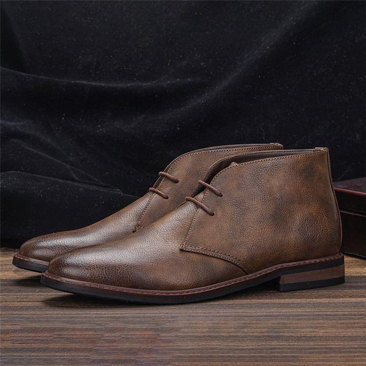 Pair of rustic brown leather lace-up chukka boots on a wooden floor with a draped black fabric backdrop.