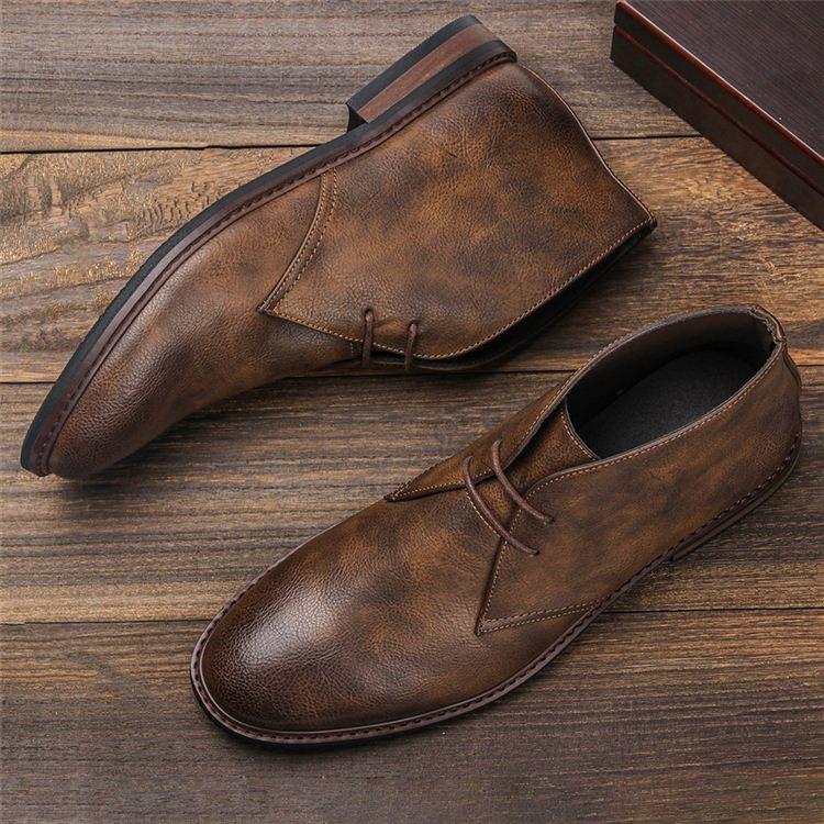 Pair of rustic brown leather chukka boots lying on wooden planks, one tipped on its side.