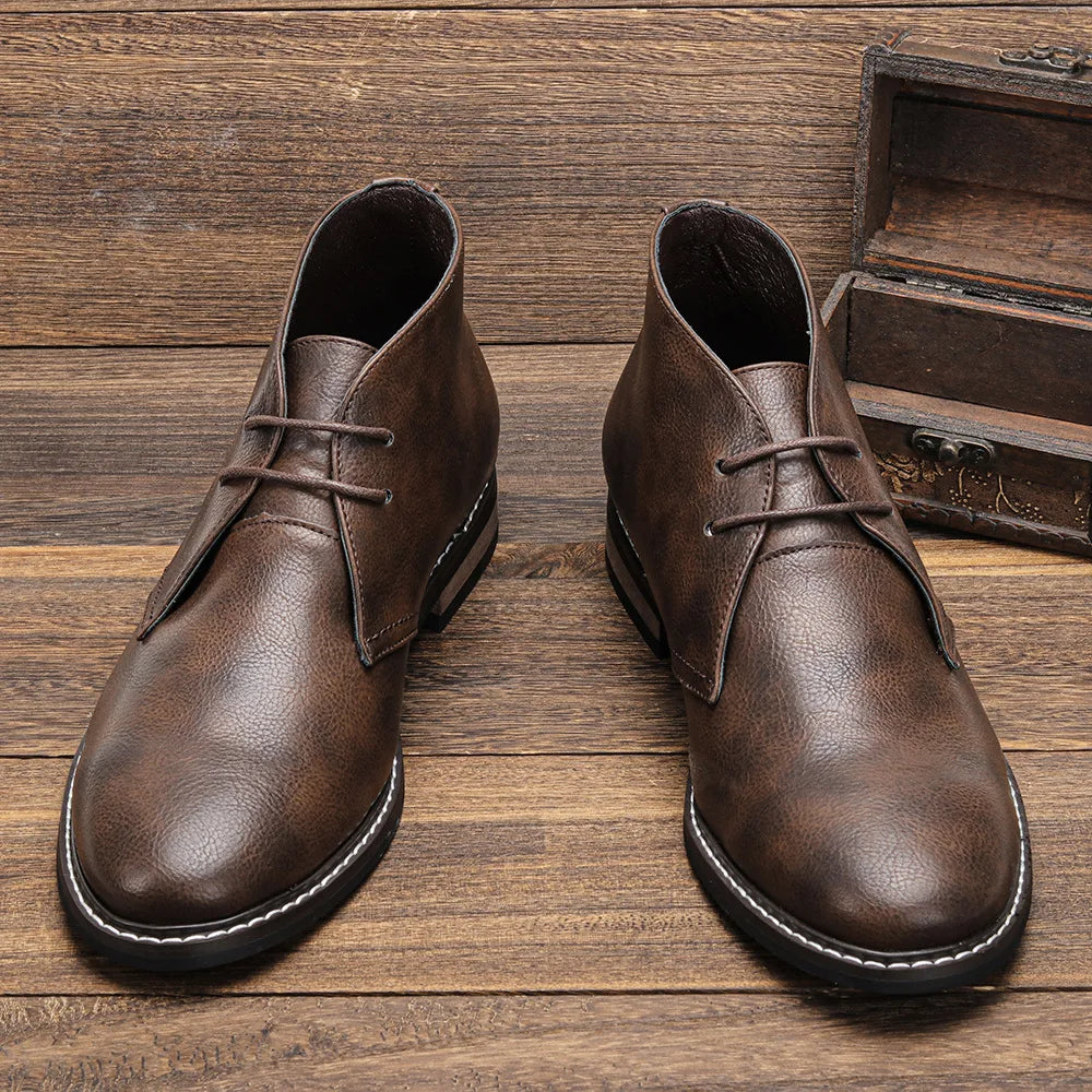 Pair of dark brown leather chukka boots standing upright on wooden steps beside a small wooden treasure chest.