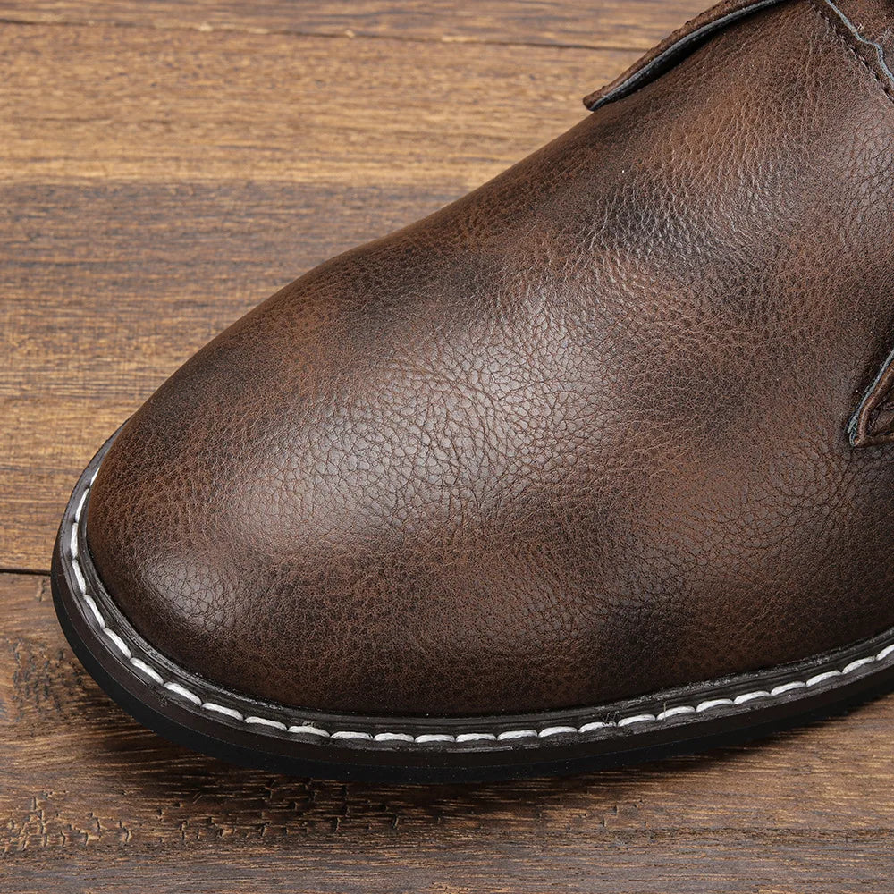 Extreme close-up of the toe and stitched sole of a dark brown leather chukka boot, resting on a wooden surface.